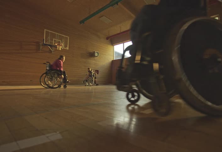Players in wheelchairs practice basketball on an indoor court and one of them catches the ball