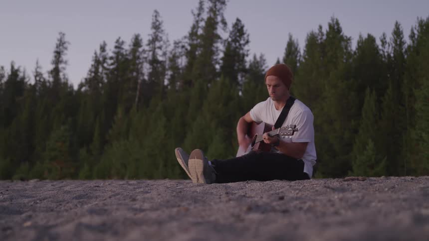 A man is sitting on the ground playing his guitar