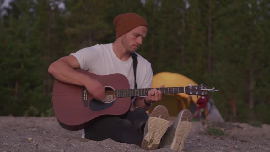 A man is strumming a guitar by his tent