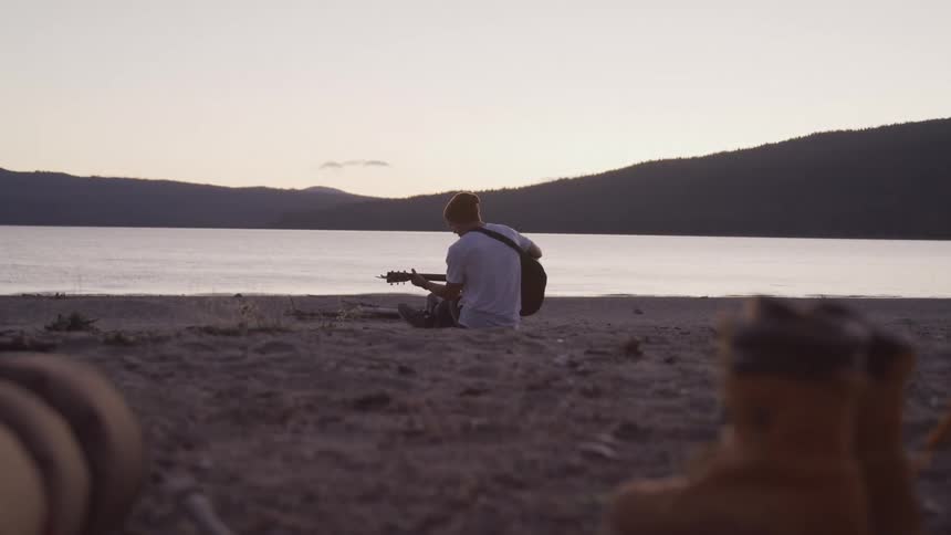 A man is playing guitar by the lake water