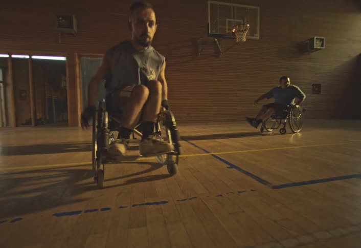 Players in wheelchairs move around a floodlit basketball court
