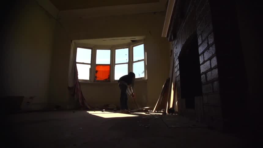 A person throws something heavy like a large mallet onto the floor inside an empty room