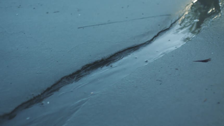 Small stream of water running over wet sand