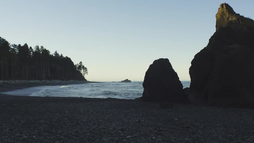 Ocean waves roll into a forested coastline at sunset