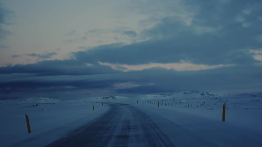 A snowcovered road stretches into a vast wintry landscape under an overcast sky