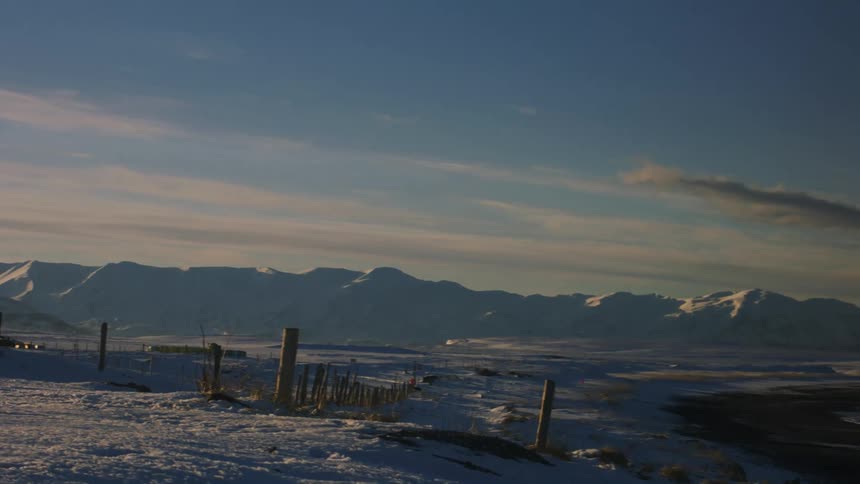 Snowcovered mountain landscape stretches out under a blue sky with elongated clouds