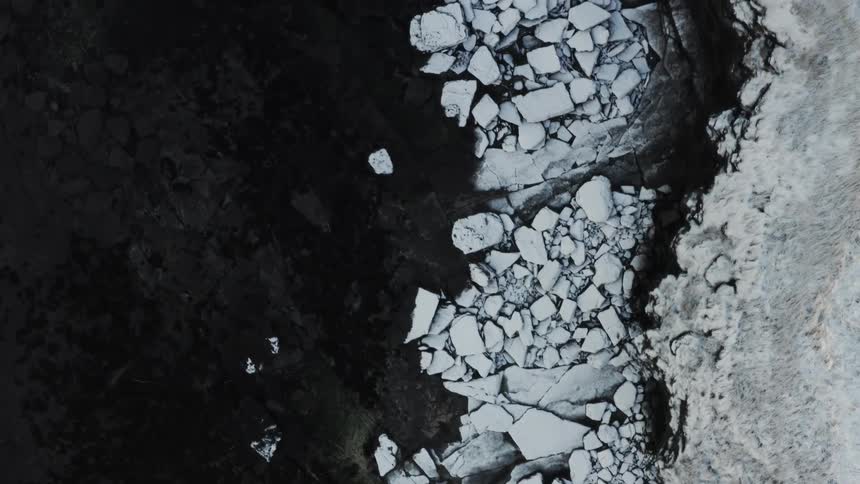 Aerial top view over a rocky coastline and cliff with snow