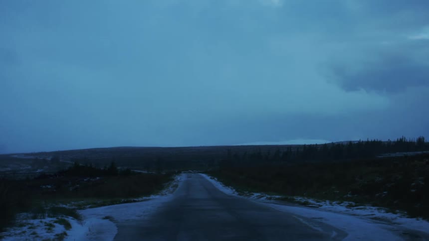 Narrow snowy road surrounded by mountains and conifers