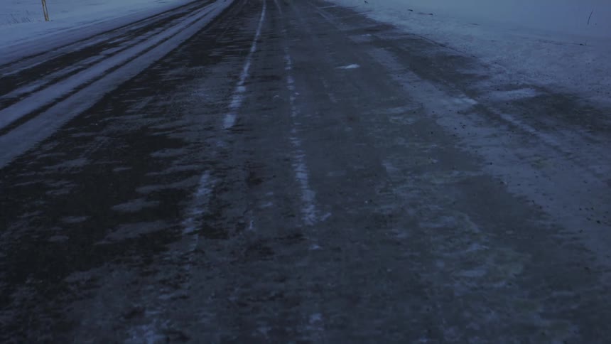 A closeup of an iced mountain road pans upward revealing a vast winter landscape with bright yellow markers on each side