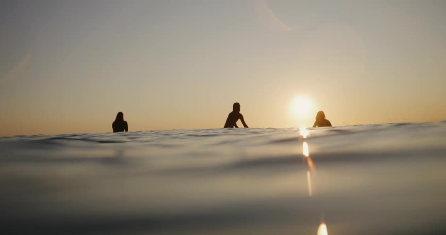 Silhouette of three female surfers in the ocean at dawn