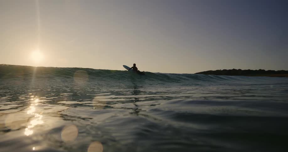 A view from underwater looking up where there is a surfer heading towards an approaching wave