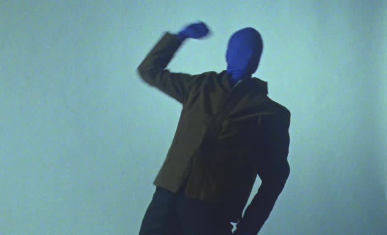 Blue man wearing brown jacket dancing against white back drop for a photo shoot