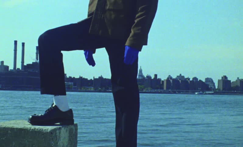 A person with their leg on top of a concrete block and wearing blue gloves and behind them a body of water and a city in the background