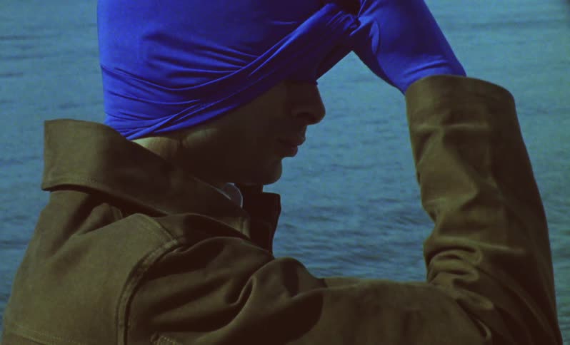 Person wearing a dark coat adjusting the blue mask covering his face
