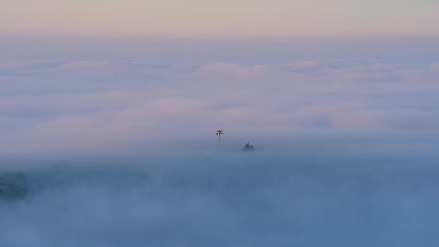 A misty cityscape nestles under a pastelcolored twilight sky partially obscured by lowlying clouds