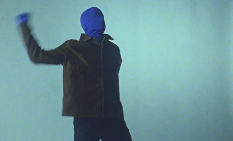 A performance artist wearing a blue mask and gloves is dancing
