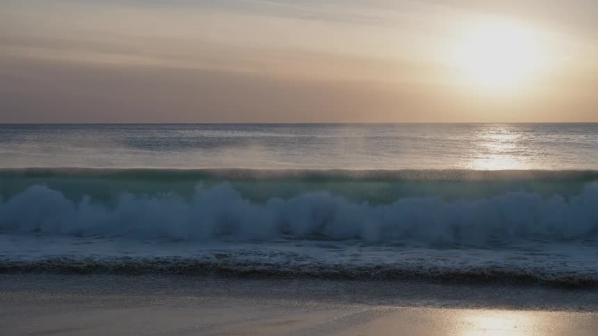 A large wave crashes on the sandy beach