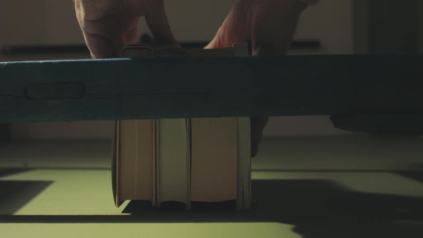 A pair of hands placing books on a shelf against a green wall