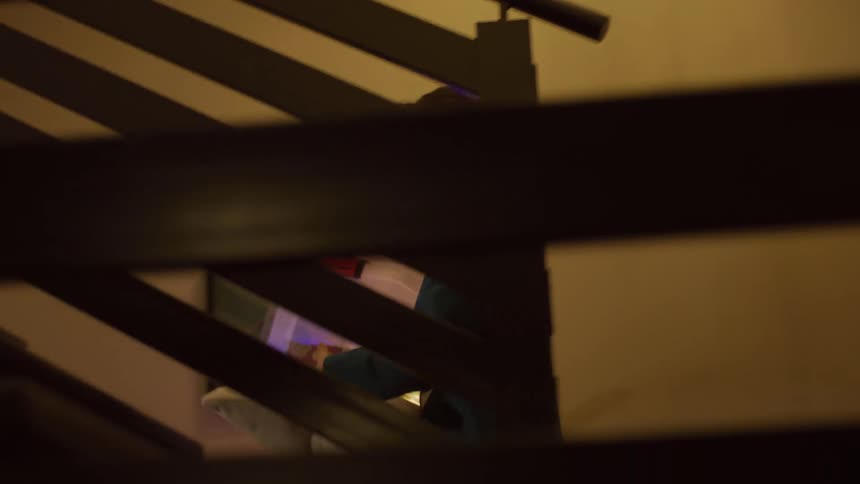 Boy walking down a staircase in a cozy house holding a pillow and a clear plastic box with colored lights inside
