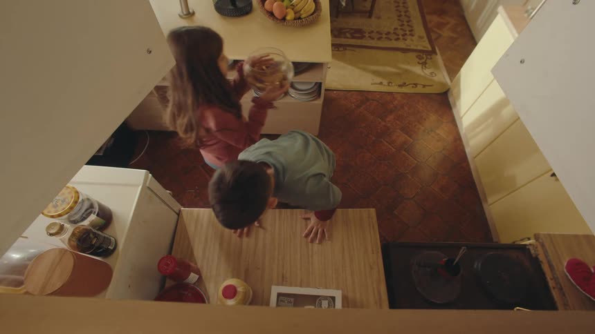 Boy picking up a glass jar of cookies and handing it to his sister next to him