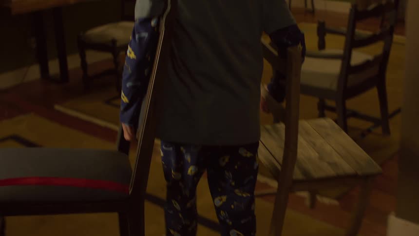 Boy carrying two chairs and carrying them across a room on a rug