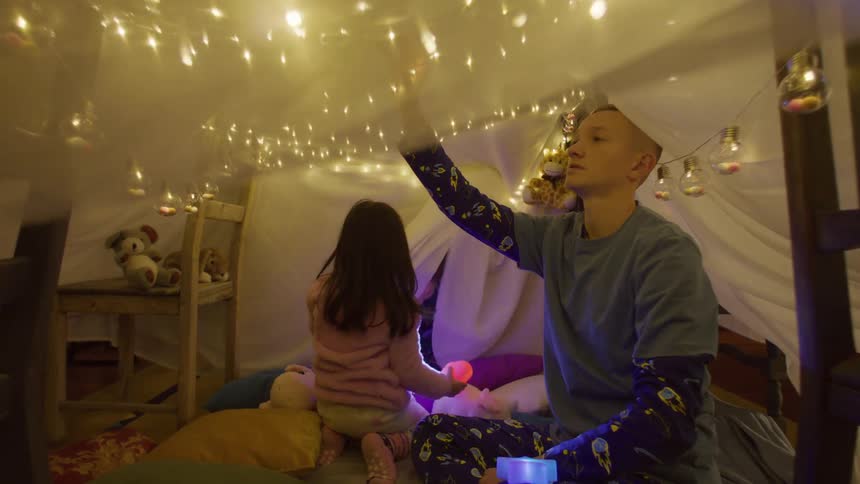 Three children playing in a sheet cabin with christmas lights
