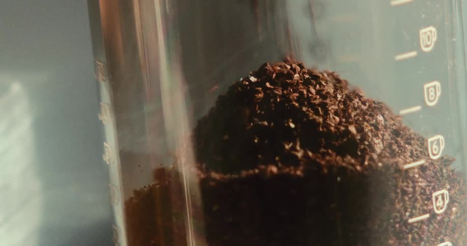 Several black grains falling into a pile on top of a glass container with markings