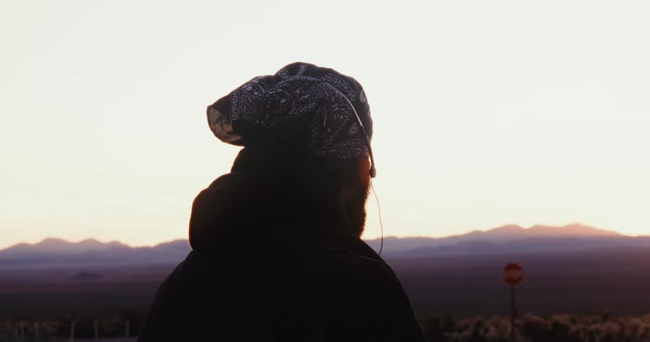 Man standing near a highway passing a patch of cholla cacti puts on headphones