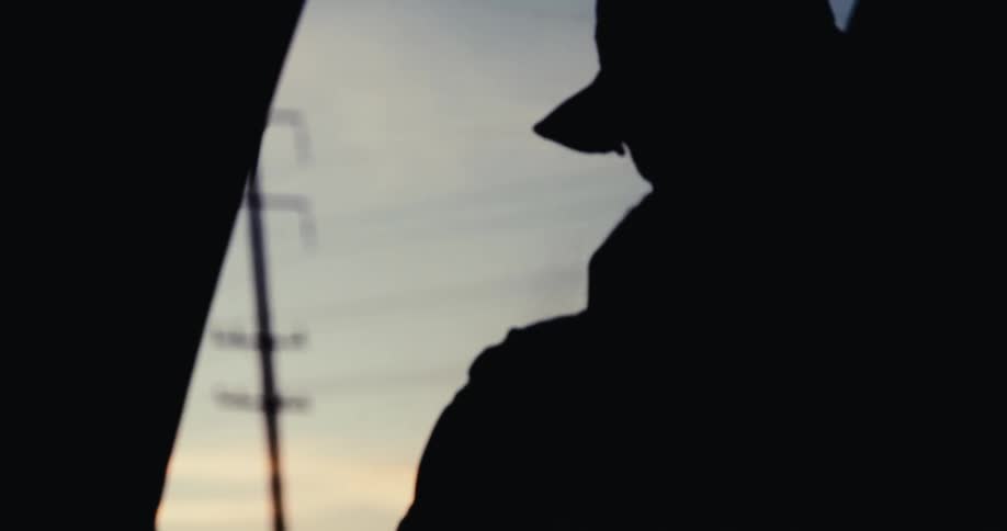 The silhouette of a persons head wearing a hat and moving on a dark morning
