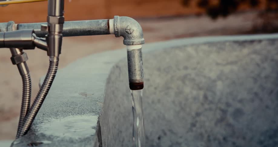 Water flows from a pipe into a basin in a desert environment