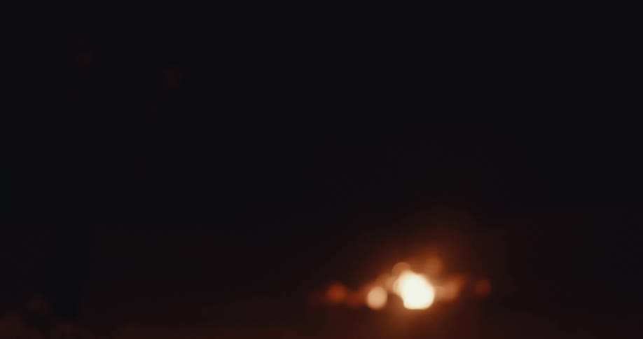 Silhouette of a person walking towards a bonfire in a natural location at night