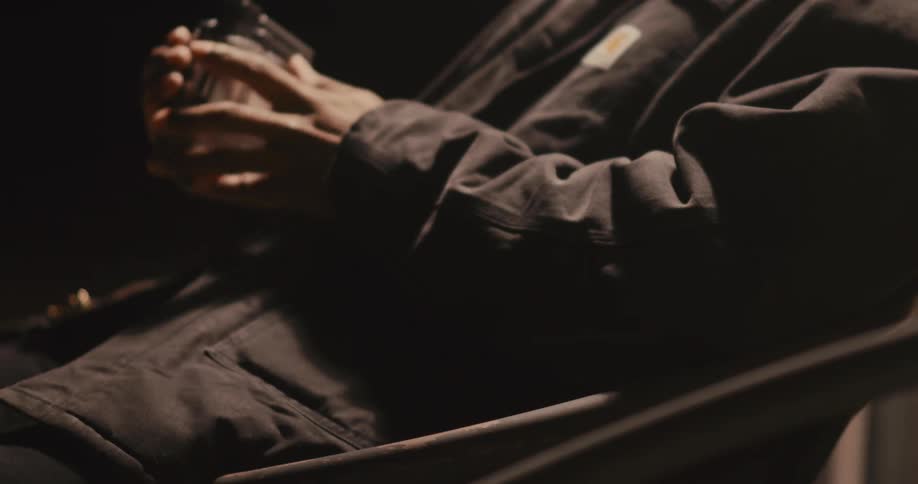 The man comes to sit down in the chair then carefully holds a handheld camera in his hands his grip firm yet contemplative