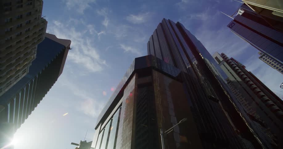 Skyscrapers with mirrored facades reflect sunlight against a blue sky with few clouds