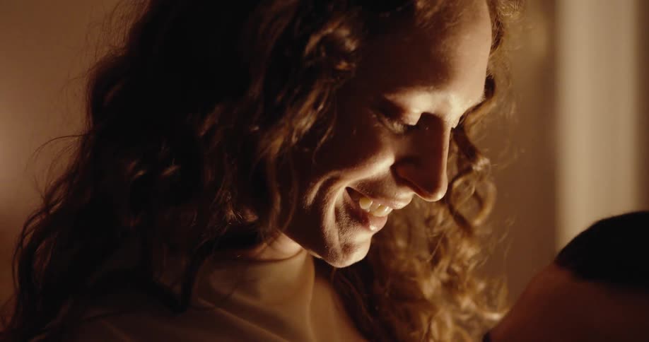 The face of a woman who is happy while she is talking to a man who is in front of her and her face is being illuminated by natural light