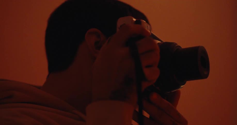 A person is looking through a camera viewfinder in a dimly lit orangehued environment