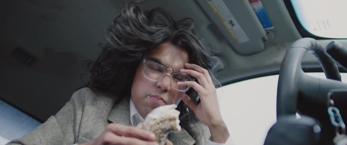 Man inside the car eating a sweet bread while dancing at the same time