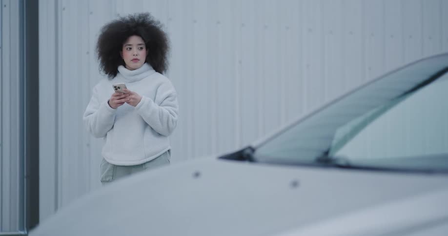 Woman walking outdoors and using her cell phone notices a car shaking nearby and continues walking