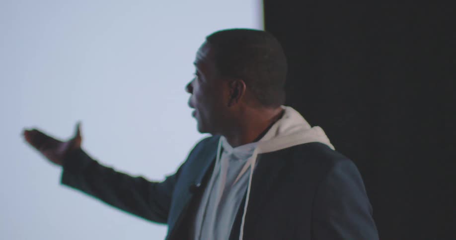 A man points towards the screen on the stage
