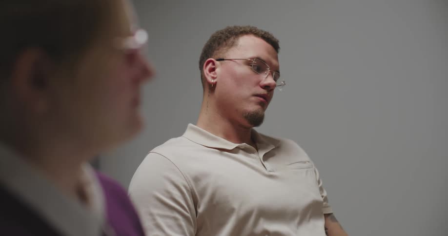 A man in a meeting room eats a pastry messily with his hands while others engage in conversation