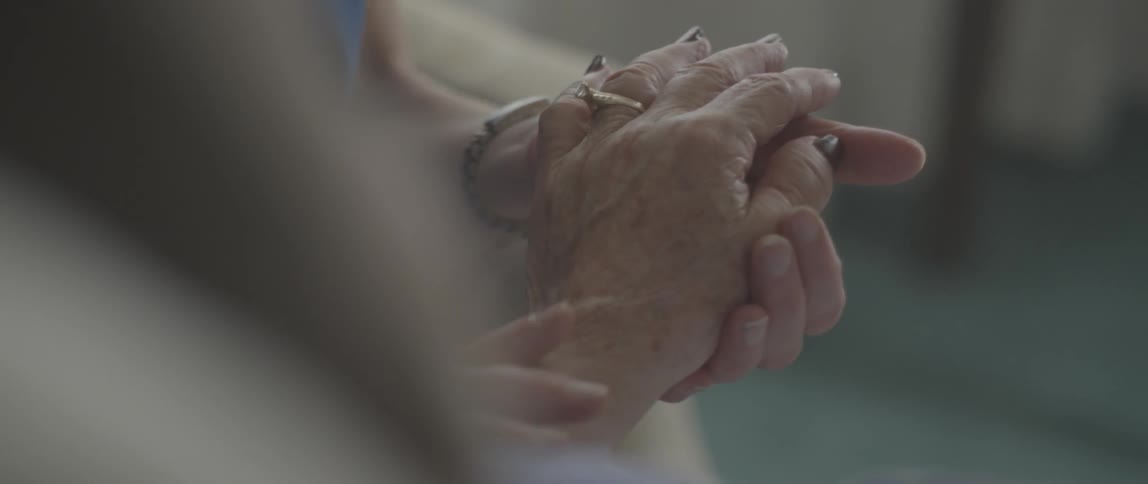 An elderly woman's hand is stroked by another person