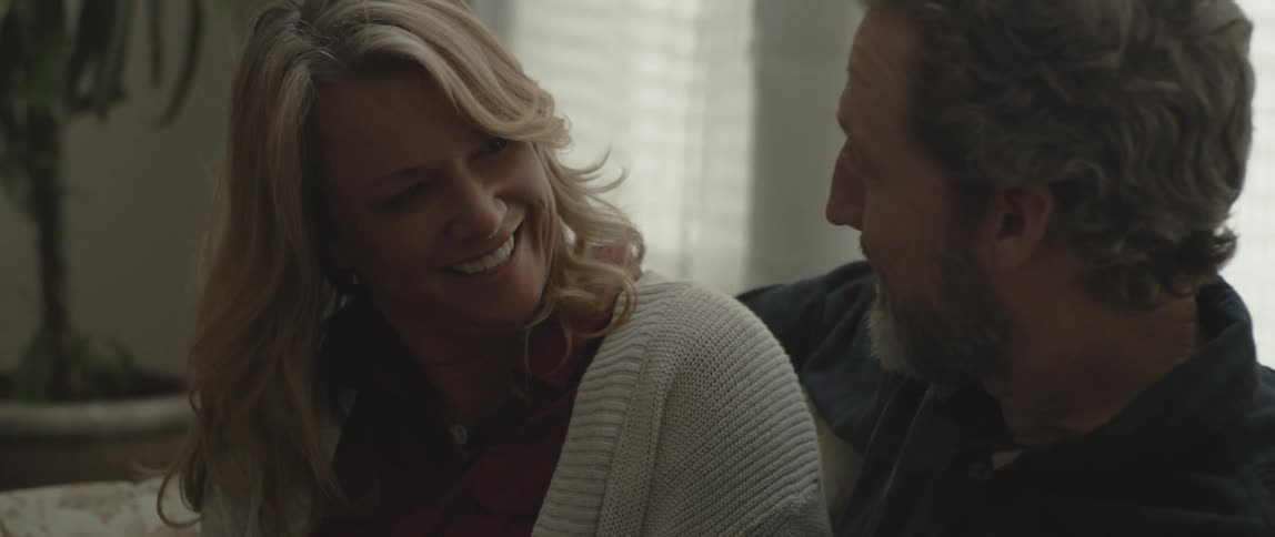 A man and woman sit on a couch talking and smiling