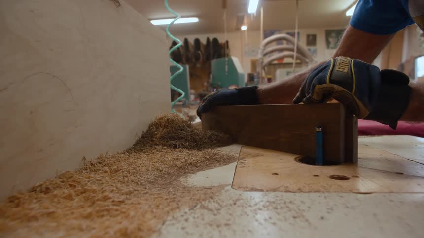 Pair of hands of a carpenter with gloves handling a piece of wood and scraping it