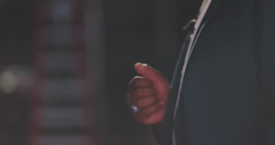 A man standing with one hand near his belly and wearing a blue suit walking forward and then he turns and some photo flashes are fired at him