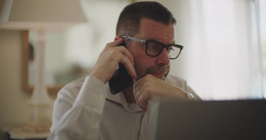 Closeup of a man talking on a smartphone while working from home with a blurred room in the background
