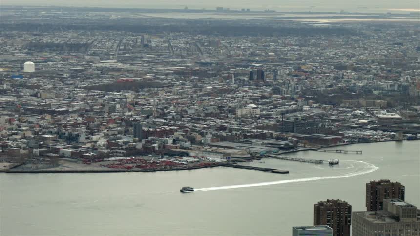 Aerial view of a large boat moving down a large river in a heavily populated area