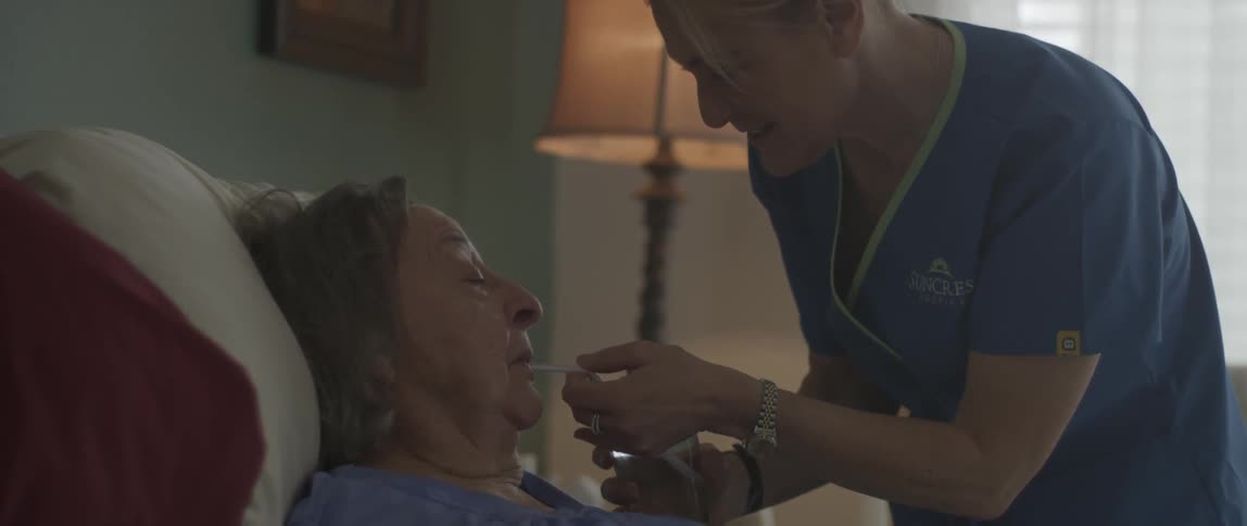 A nurse gives an elderly woman a sip of water