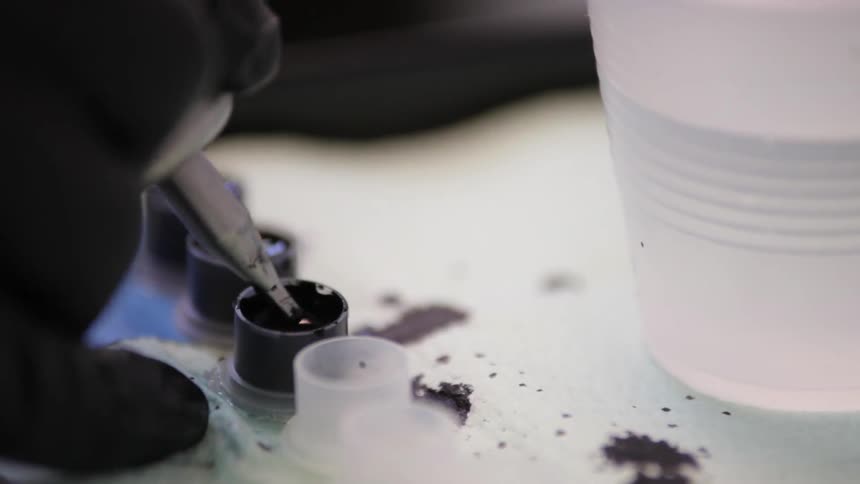 Person dipping an instrument into ink and splashing off excess