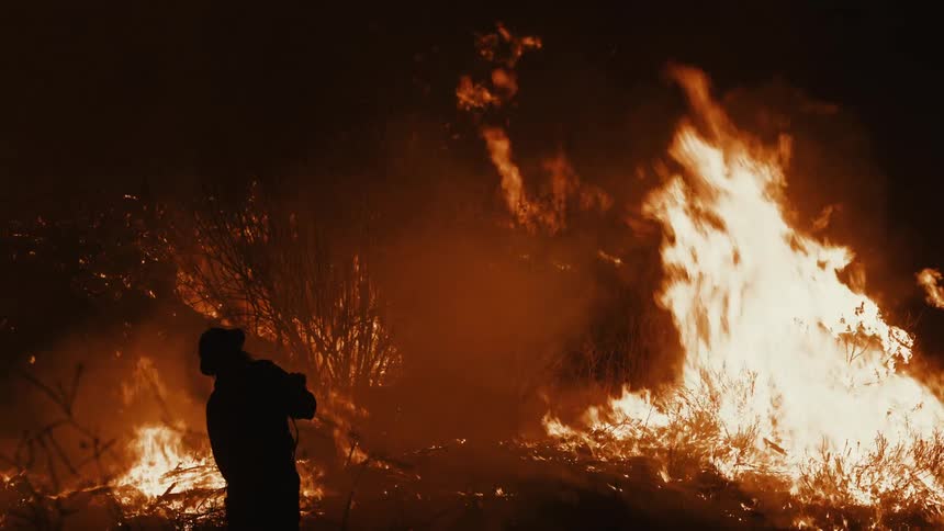 Firefighters battle a forest fire surrounded by intense flames and thick smoke