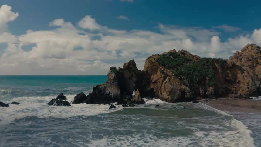 Aerial view of a beach with the rocky coastline in the background