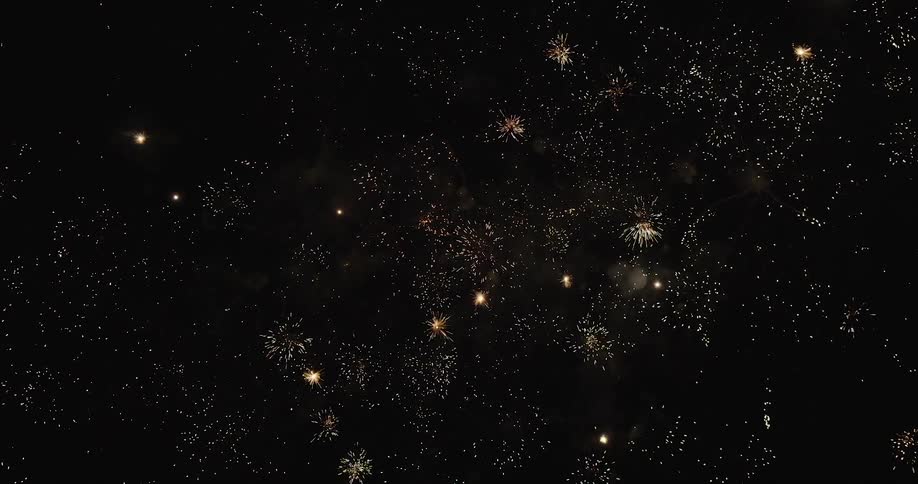 Multiple fireworks explode overhead filling the night sky with dazzling colors and rocket trails
